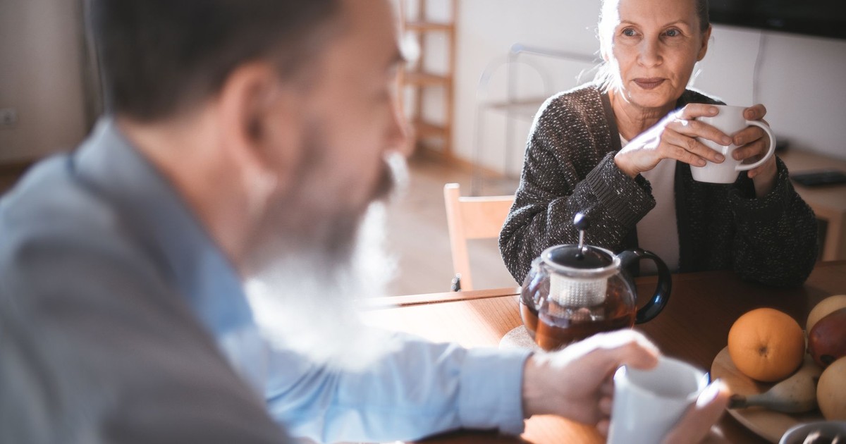 Elderly man and woman sharing a coffee moment in a cozy indoor setting.