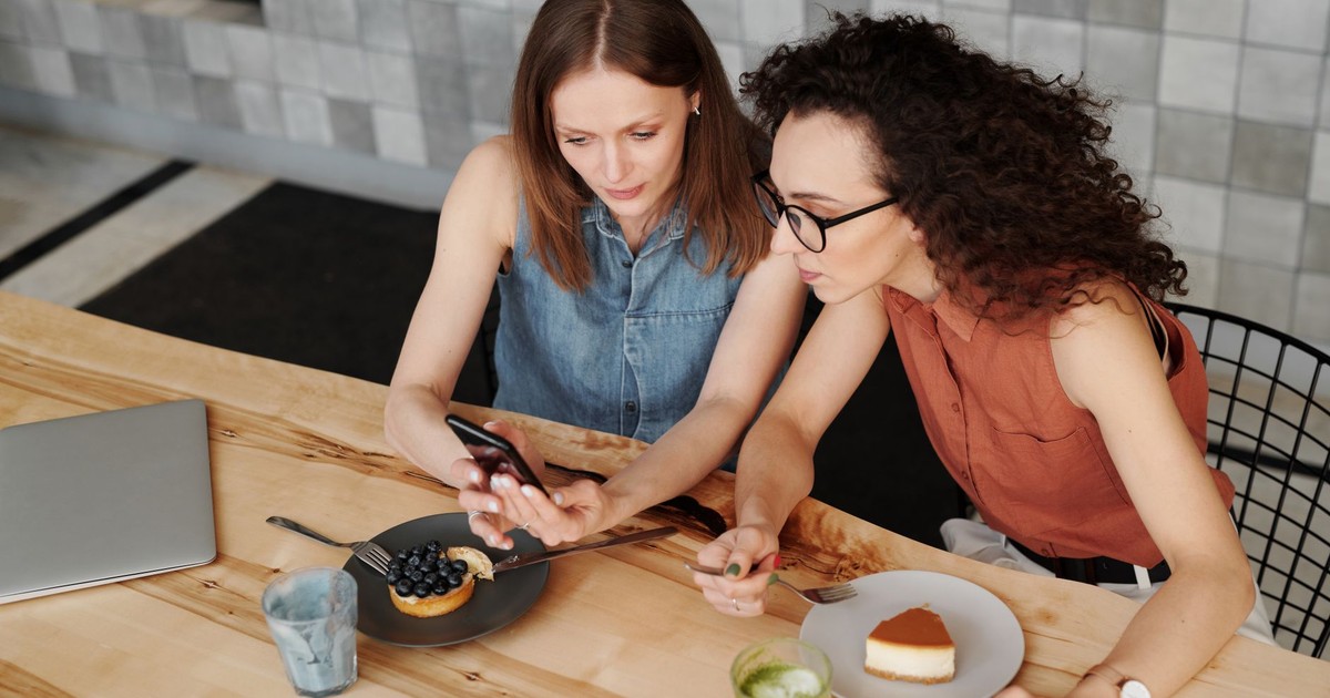 Two women enjoying desserts and using a smartphone at a cozy café.