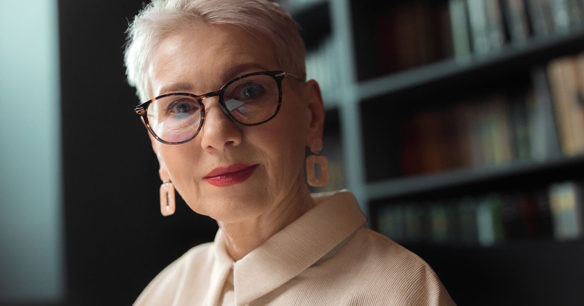 A sophisticated elder woman with glasses in a library setting, exuding elegance.