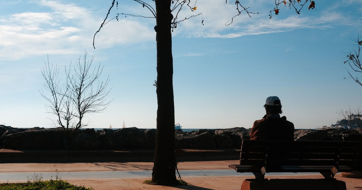 An individual sitting alone on a bench by the sea, embracing solitude in autumn.
