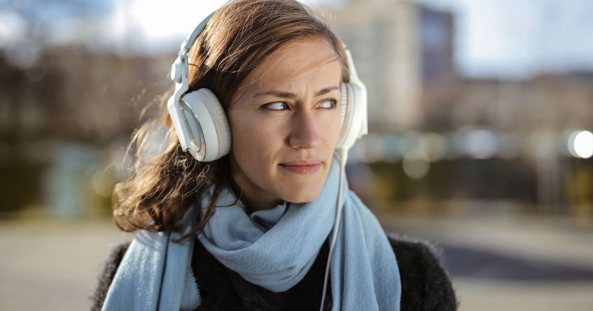 Young woman with headphones and scarf enjoying music outdoors on a sunny winter day.