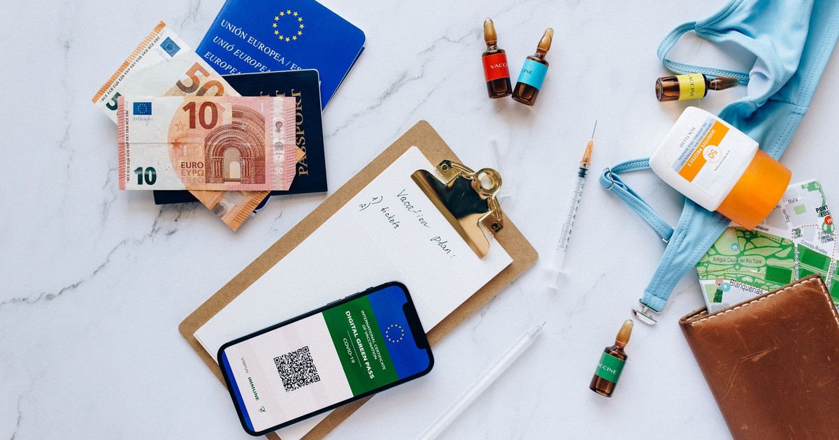Flat lay of travel essentials including vaccination passport, euros, and medical supplies.