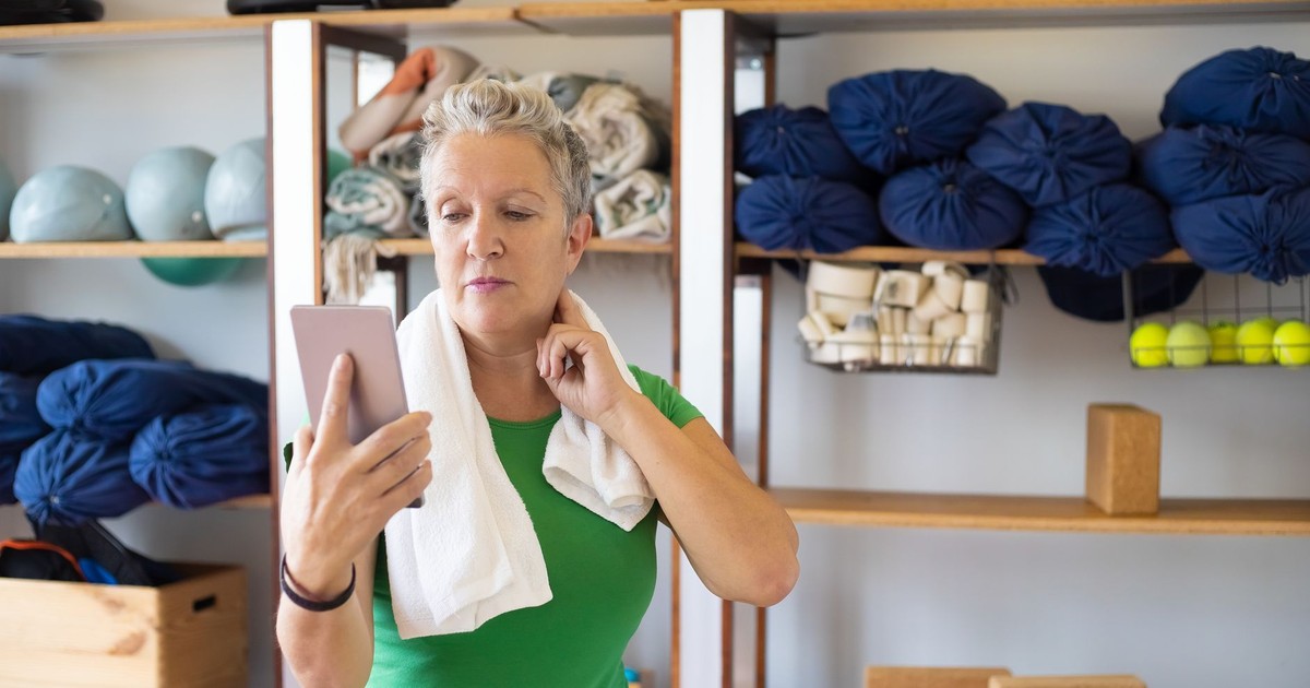 Woman in green shirt checks fitness tracker in yoga studio, emphasizing health and wellness.