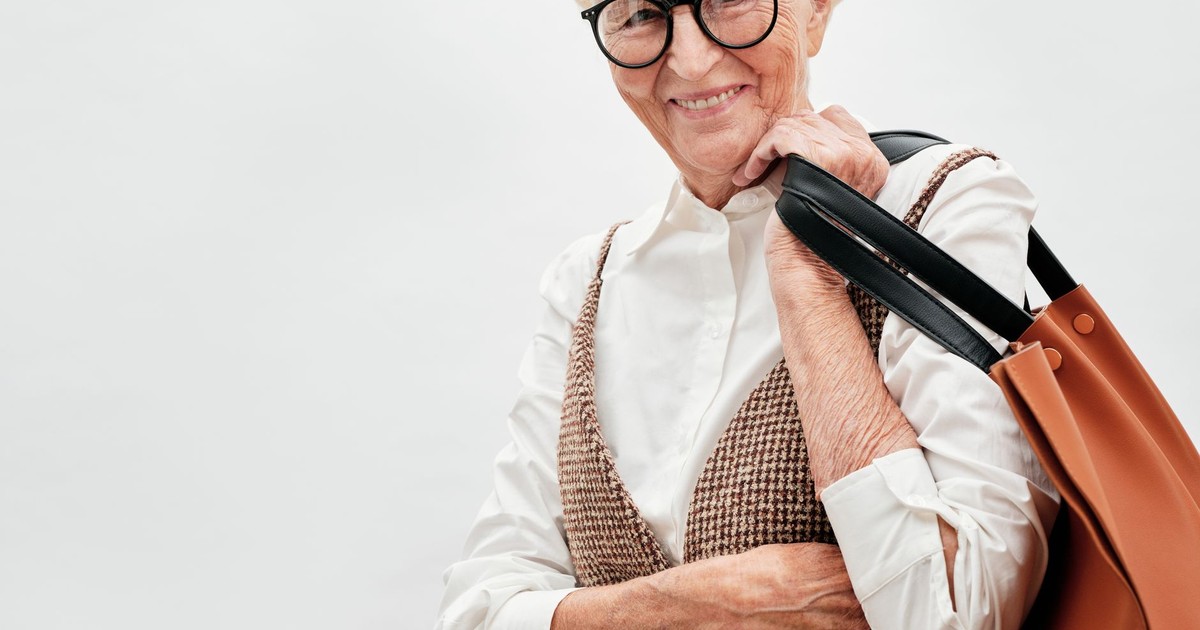 Chic senior woman in eyeglasses holding a shoulder bag, smiling confidently.