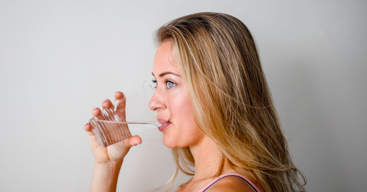 Side view of a woman with blonde hair drinking water from a clear glass.