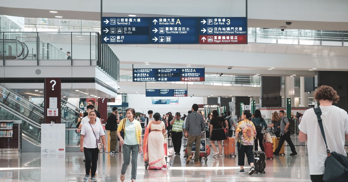 Crowded Hong Kong airport terminal with diverse passengers and informative signage.