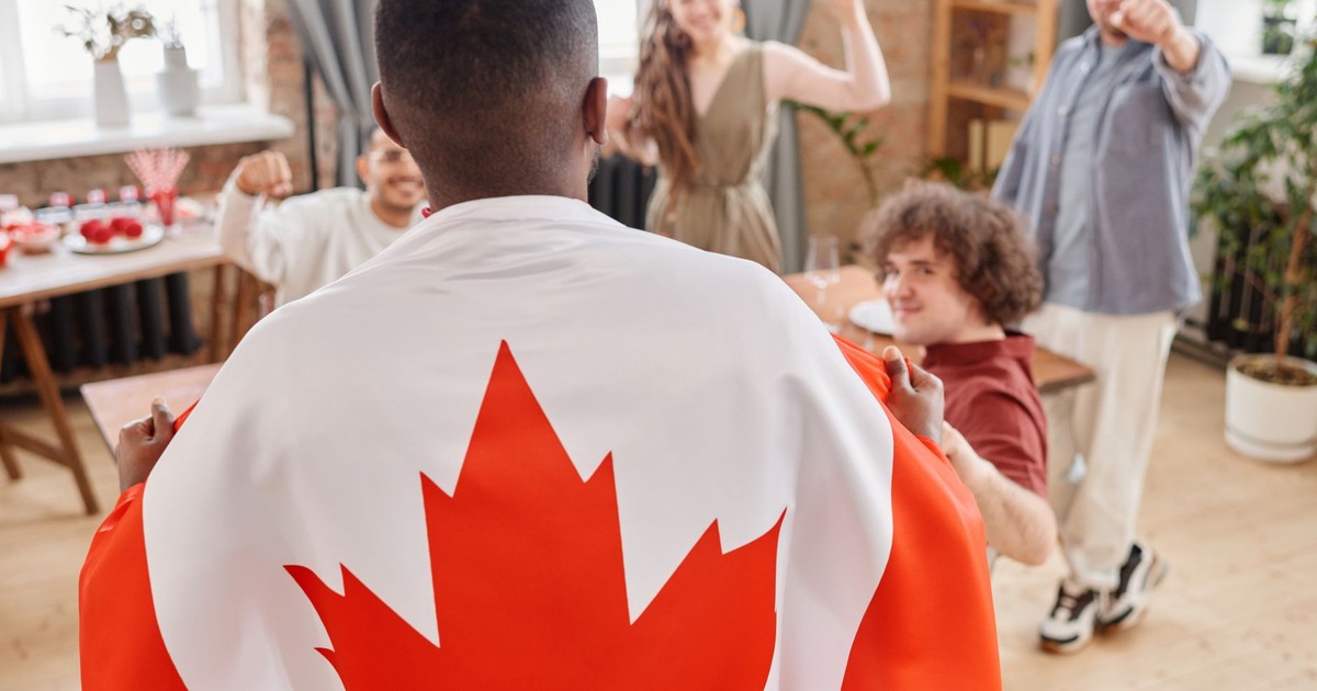 Group of friends celebrating Canada Day indoors with a Canadian flag draped over one person.