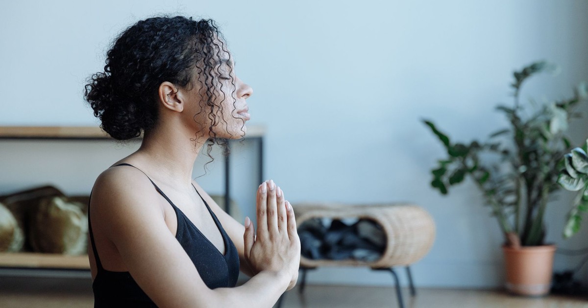 A serene woman in black attire meditates in a calm indoor setting, promoting wellness.