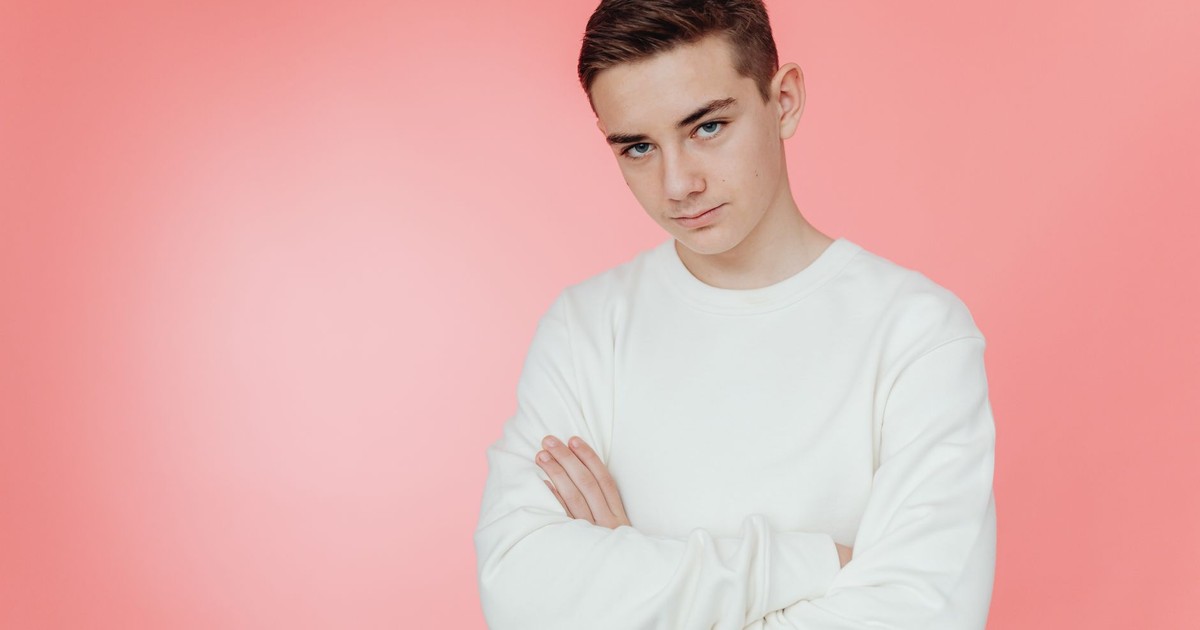 Confident teenage boy with arms crossed against pink background.
