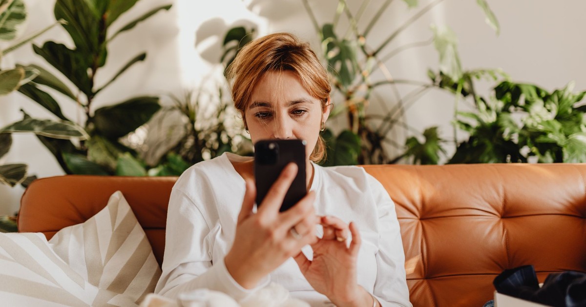 Woman in casual setting, using a smartphone on a sofa with indoor plants.