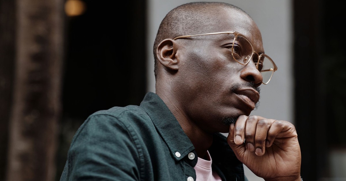 Thoughtful man with glasses sitting outdoors in contemplation.
