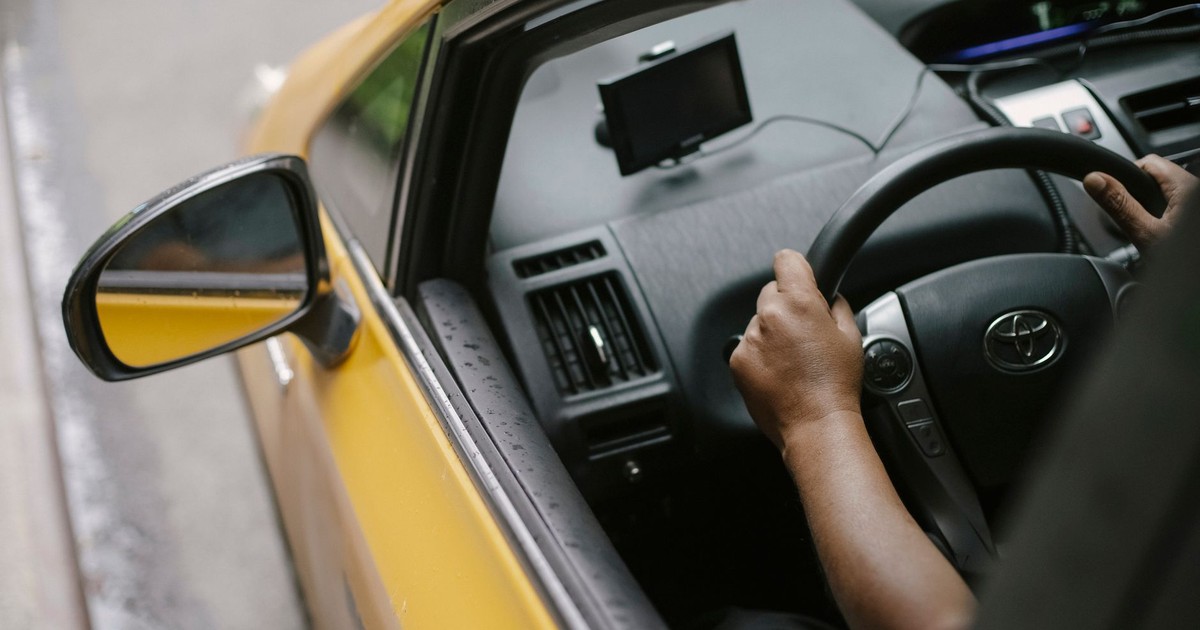 From above of crop unrecognizable person driving modern yellow taxi car with GPS navigator on city street in daytime