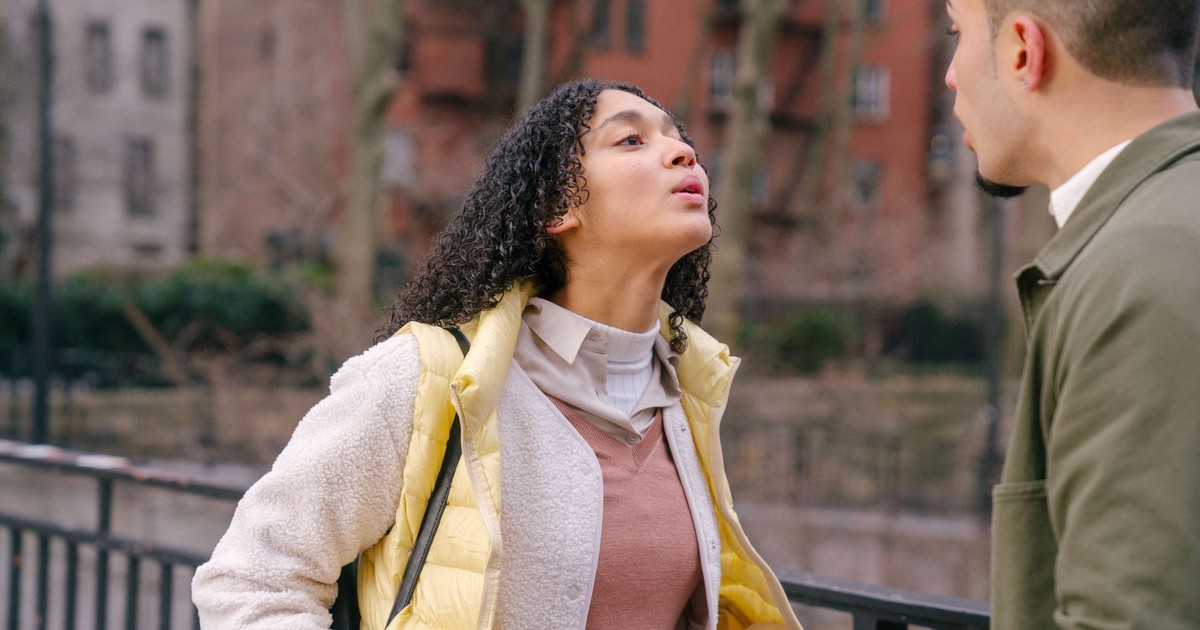Hispanic female with black curly hair in casual clothes standing and having fight with boyfriend on street in daylight
