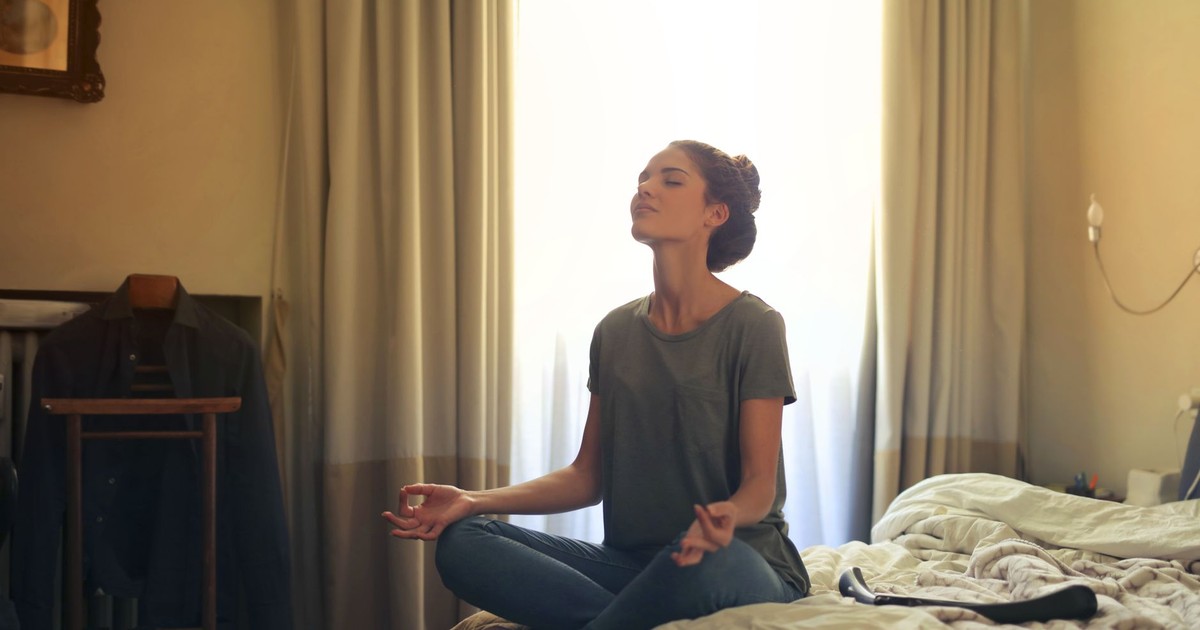 Adult woman practicing meditation on her bed surrounded by a calm bedroom atmosphere.