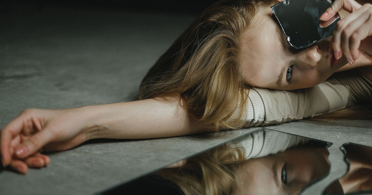 Artistic portrait of a woman lying on the floor holding a broken mirror.