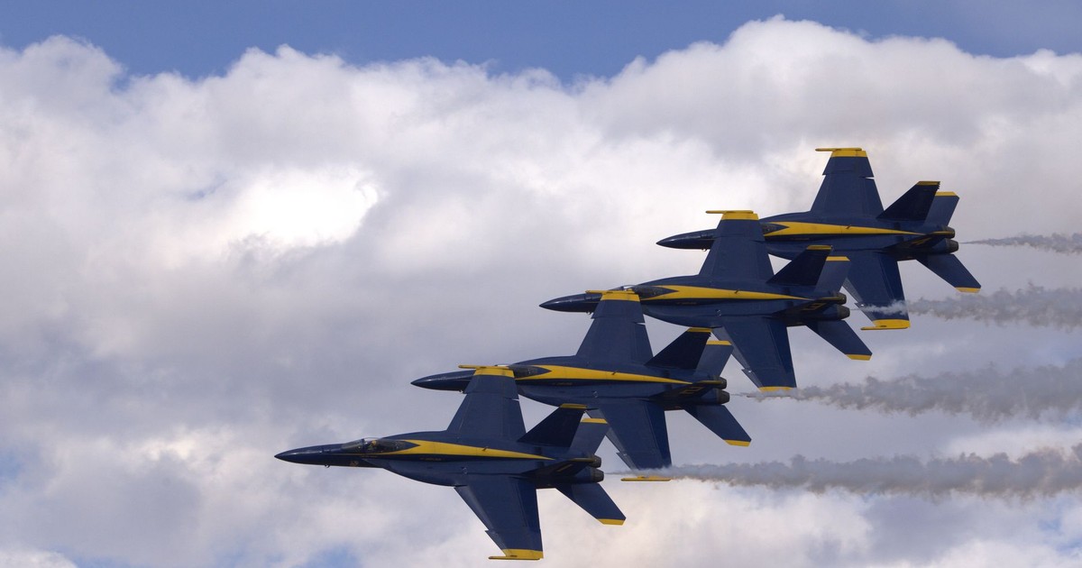 Four military jets performing an aerial formation against a blue sky with clouds.