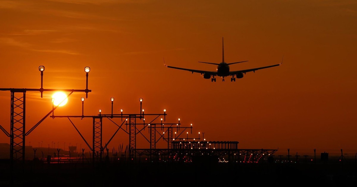 Silhouette of an airplane landing during sunset at Barcelona airport, with a vibrant orange sky.