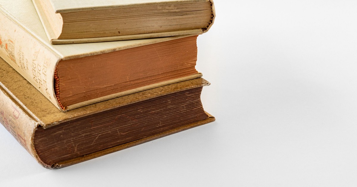 A close-up of three vintage hardbound books stacked on a white surface, showcasing their aged textures.