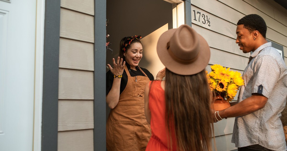 Friends surprising a hostess with sunflowers at the doorway, sharing smiles and joy.