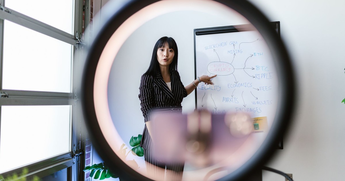 An Asian woman explaining blockchain concepts using a whiteboard, viewed through a ring light.