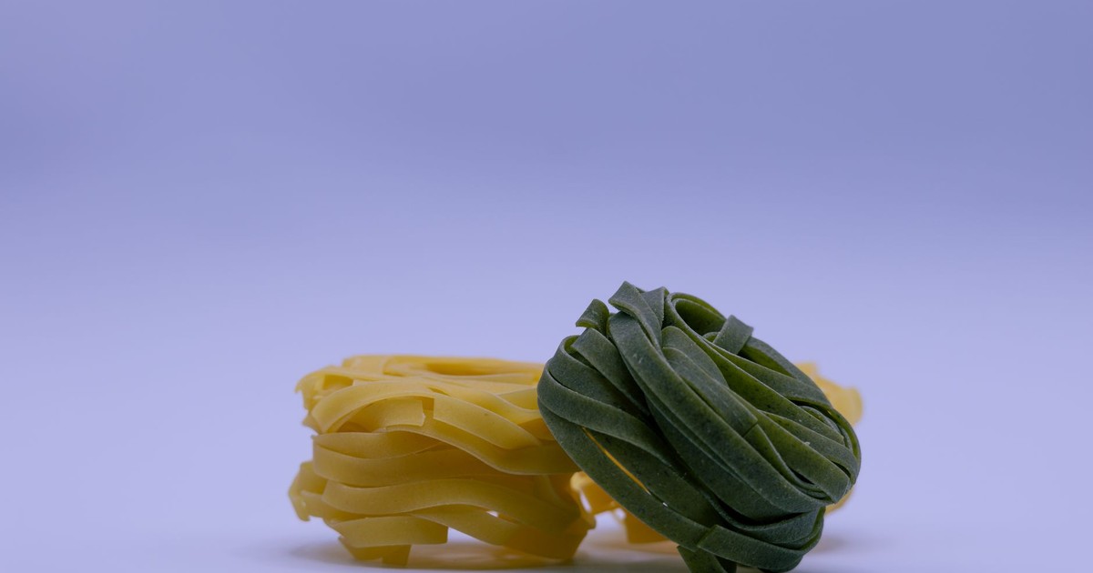 A close-up image showcasing raw yellow and green tagliatelle pasta bundles on a plain background.