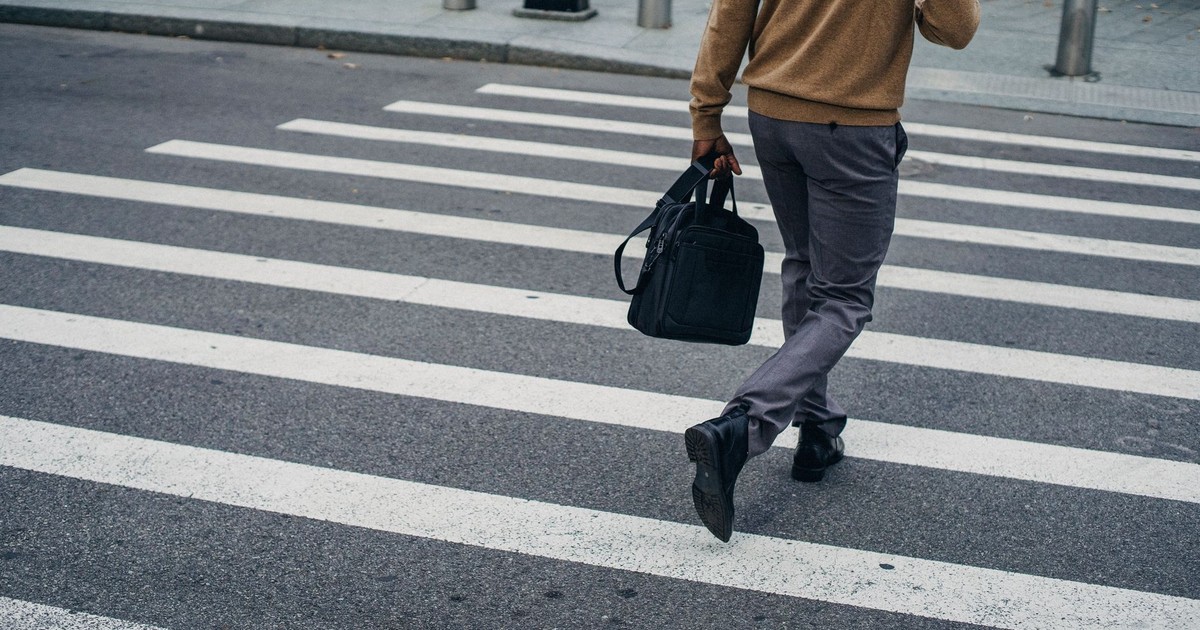 Crop back view of black male pedestrian with bag on crosswalk in city center
