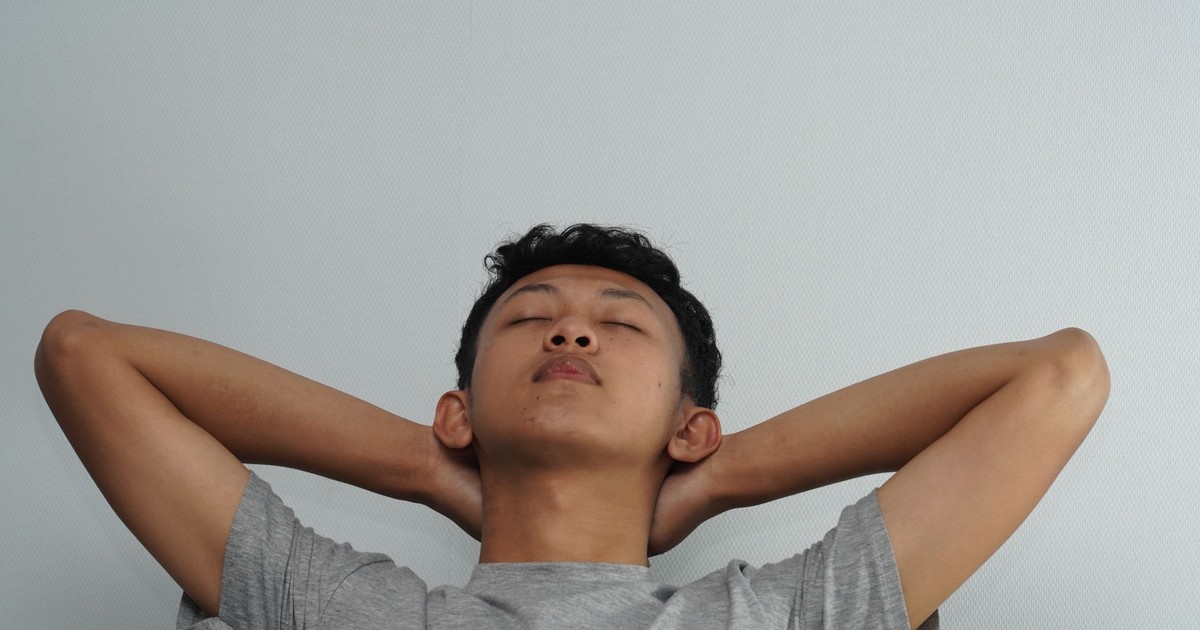 Young man relaxing with hands behind head against a plain background.