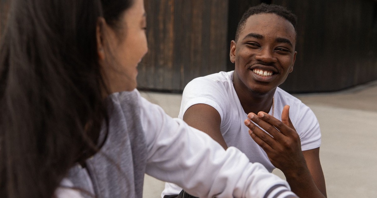 Cheerful young African American guy in casual clothes smiling while chilling on street with crop Asian female friend