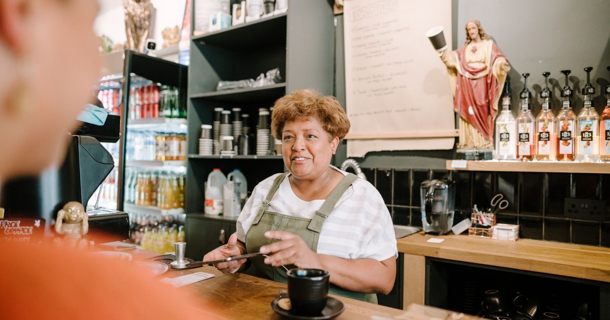 Friendly barista preparing coffee, engaging with customer in a cozy café setting.