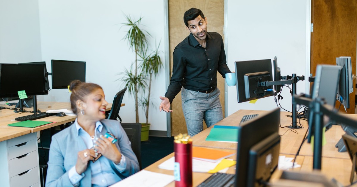 Two colleagues engaging in a cheerful conversation in a modern office setting.