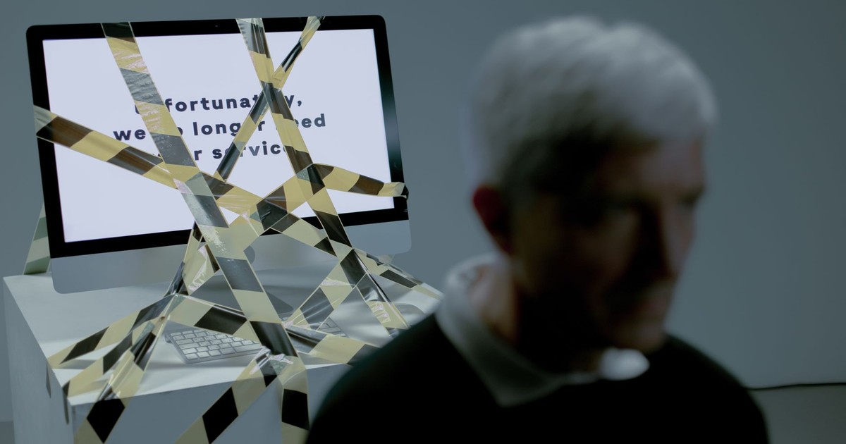 A senior man facing the reality of unemployment highlighted by a computer screen and warning tape.