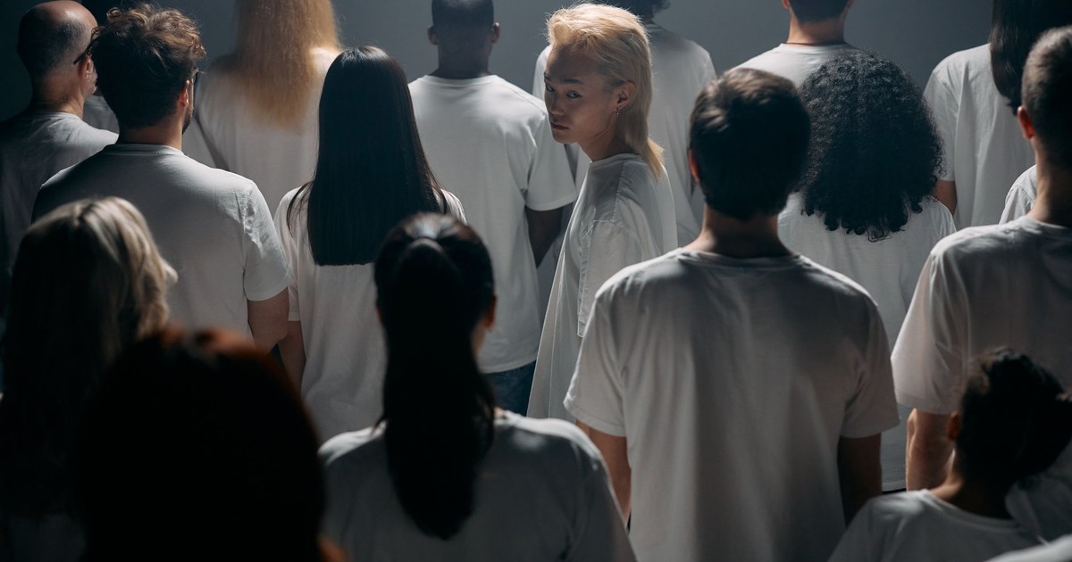 A diverse crowd stands together in a studio, exploring themes of individuality and social connections.