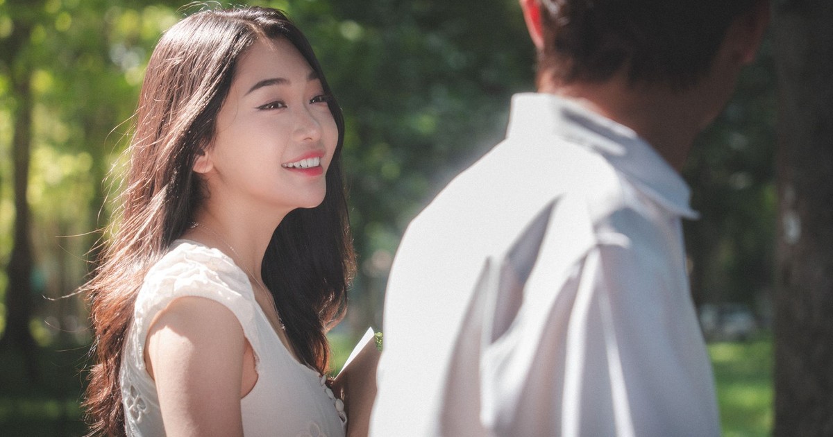 A candid moment of a young couple smiling in a sunlit park setting.