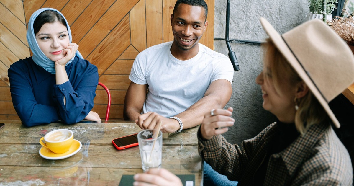 Three friends casually chatting and enjoying coffee at a cozy indoor cafe.