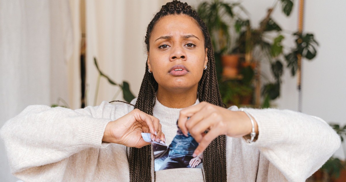 A young woman expressing emotion by tearing a photograph in a cozy indoor setting.