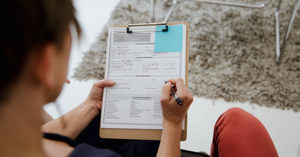 An adult woman writing on a counseling form during a business appointment in an office setting.
