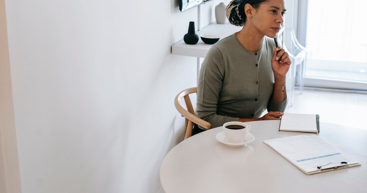 Concentrated ethnic female HR interviewer or psychologist in formal clothes sitting at round table with pen and notepad while looking away in contemplation