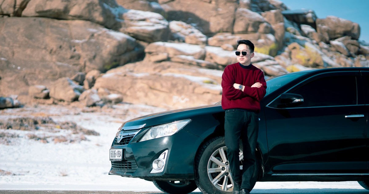 A stylish young man in sunglasses stands by a luxury black car with a rocky winter backdrop.