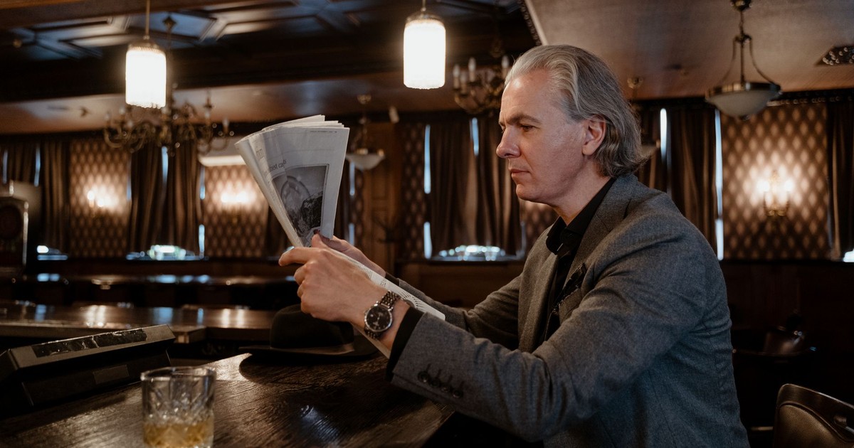 Mature man in formal attire enjoying newspaper at vintage bar counter with ambient lighting.