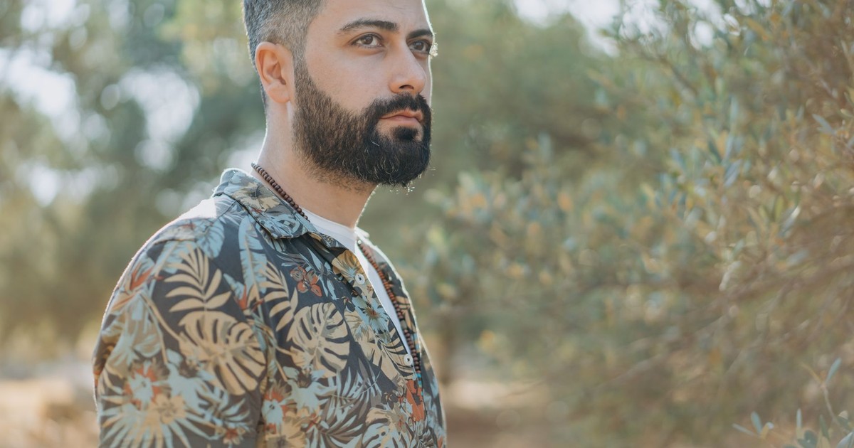 Photo of a stylish man with a beard in a floral shirt, surrounded by nature, during a summer day.
