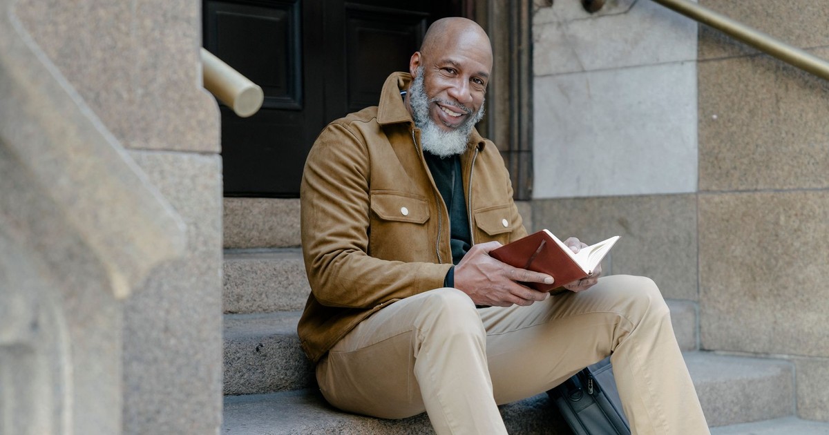 Smiling man with beard and mustache on steps holding an open notebook.