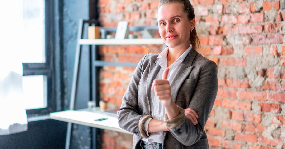 Professional businesswoman giving thumbs up in a stylish office with brick walls.