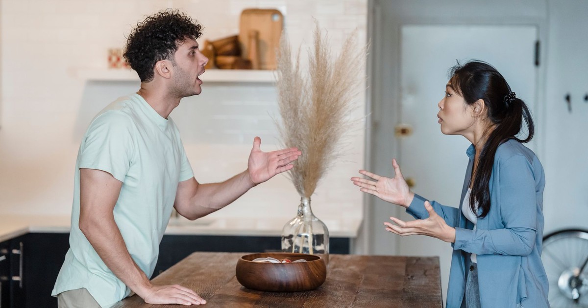 A couple engages in a heated argument at a wooden table in a modern indoor setting.