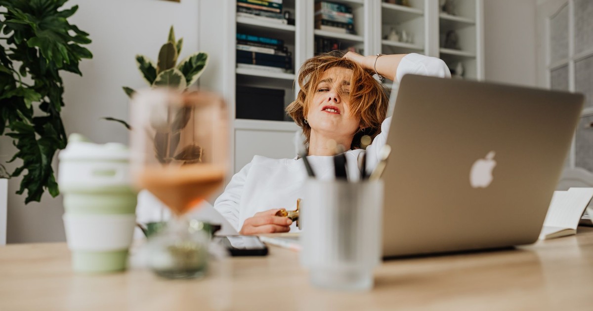 Woman feeling stressed while working from home at a desk with a laptop.