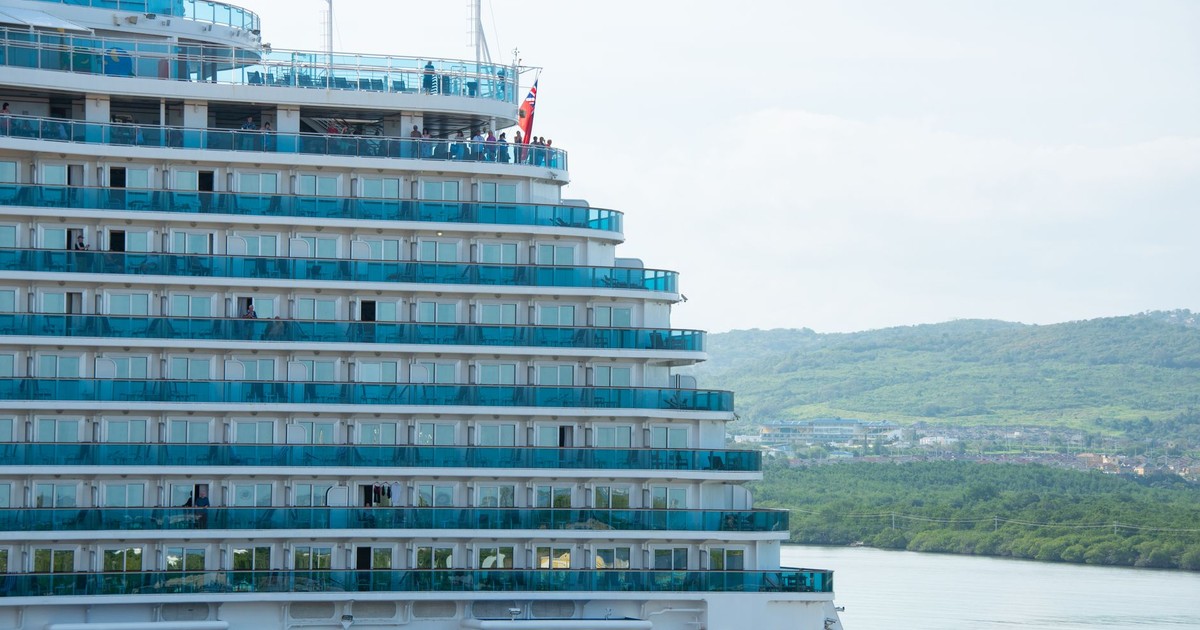 Luxury cruise ship with balconies docked by a lush green coastline, ideal for travel imagery.
