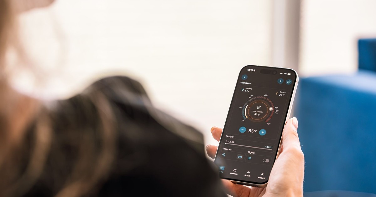 A woman holding a smartphone displaying a sauna control app, highlighting modern sauna technology.
