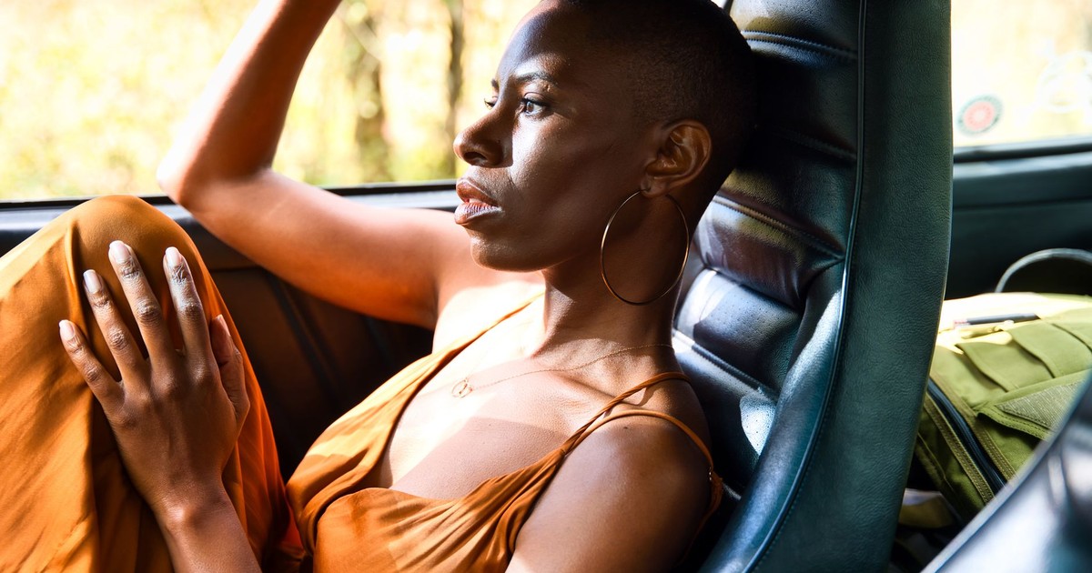 A woman in a car gazes contemplatively out the window with sunlight highlighting her figure.