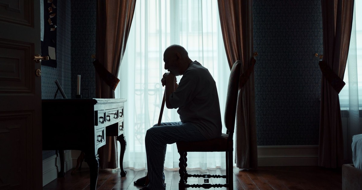 Silhouette of an elderly man sitting indoors by a window, contemplating life.