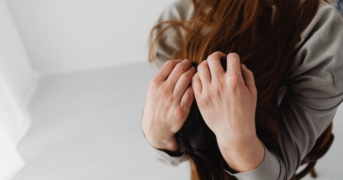 Overhead view of a woman with long hair grasping her head, depicting stress and emotion.