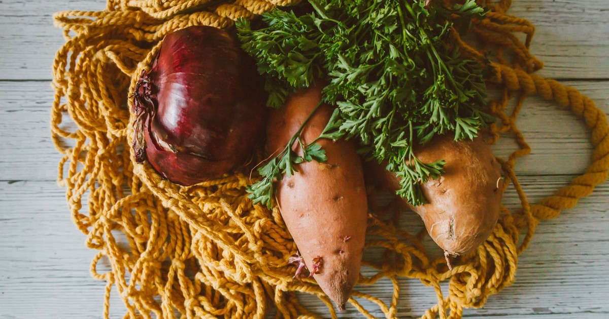 Close-up of fresh sweet potatoes and red onion with parsley on rustic background.